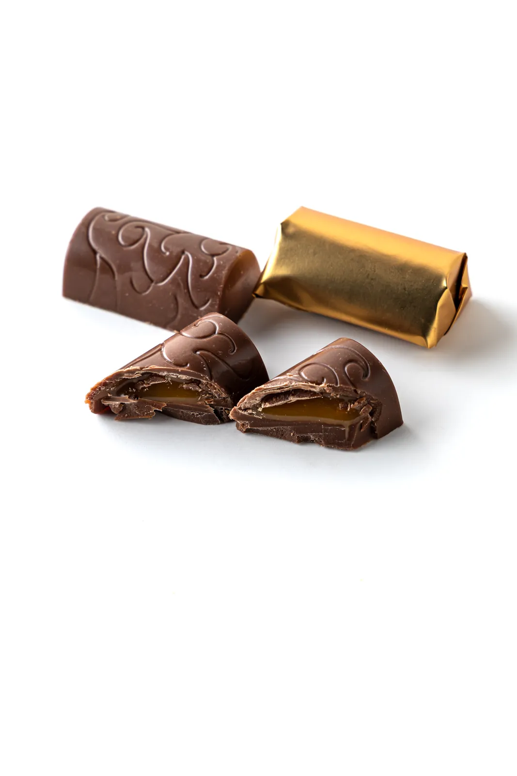 Scroll-embossed chocolate bonbons, one cut open to show a golden caramel center