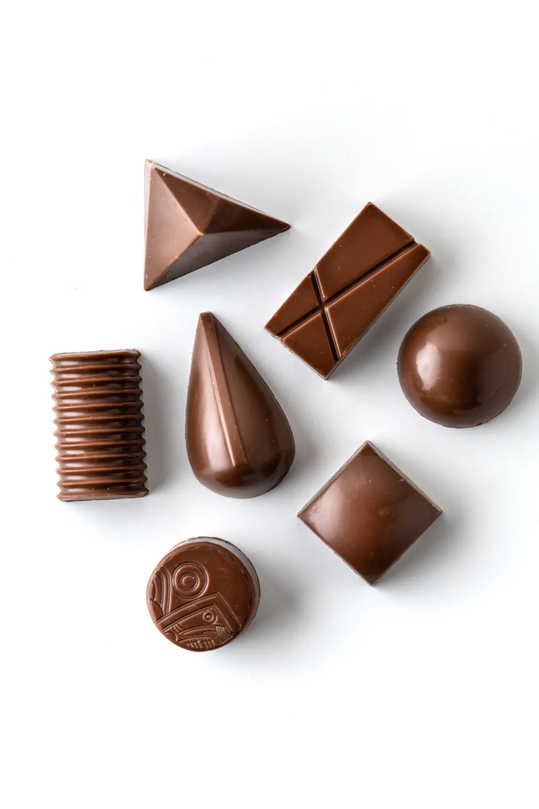 Seven geometric chocolate bonbons in assorted shapes on a white background